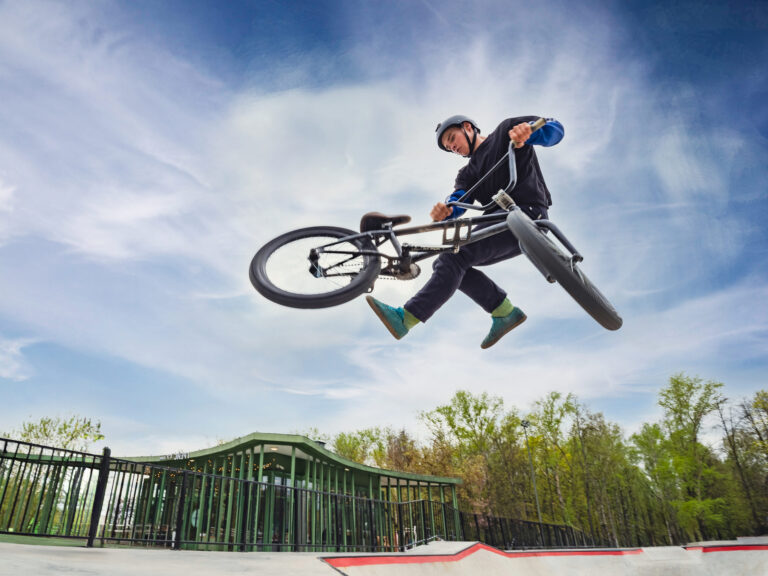 BMX bicycle rider doing stunt Tailwhip in quarter pipe. Skilled BMX freestyler athlete jumping over quarter ramp and doing aerial trick Tailwhip in street ramp park outdoors